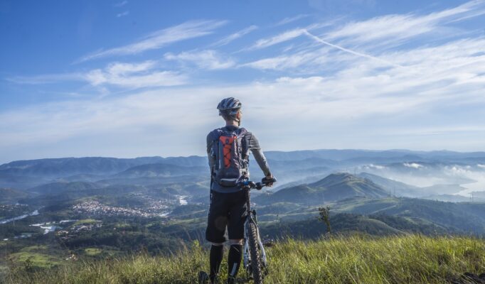 biker-holding-mountain-bike-on-top-of-mountain-with-green-161172